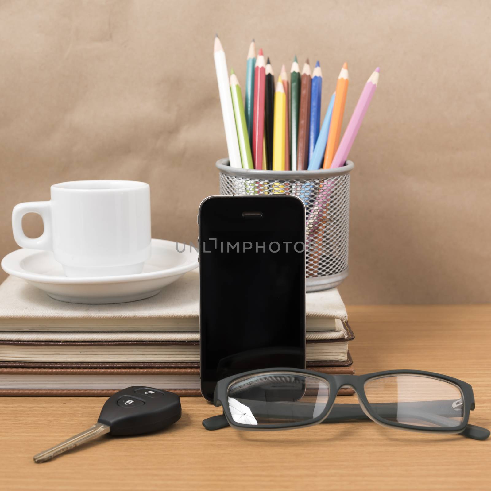 office desk : coffee and phone with car key,eyeglasses,stack of book,pencil box