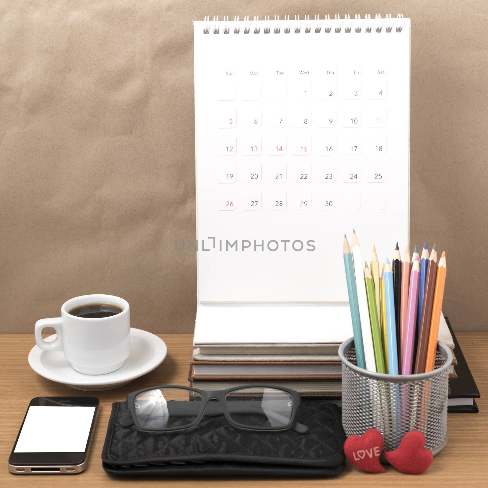 office desk : coffee with phone,wallet,calendar,color pencil box,stack of book,heart,eyeglasses on wood background