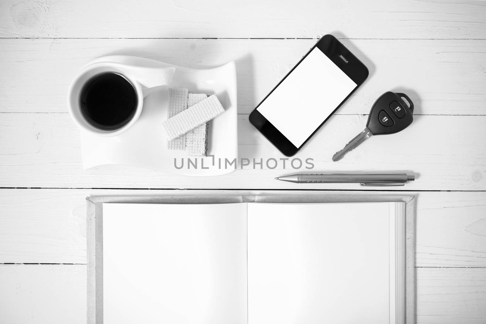 coffee cup with wafer,phone,car key,notebook on white wood background black and white color