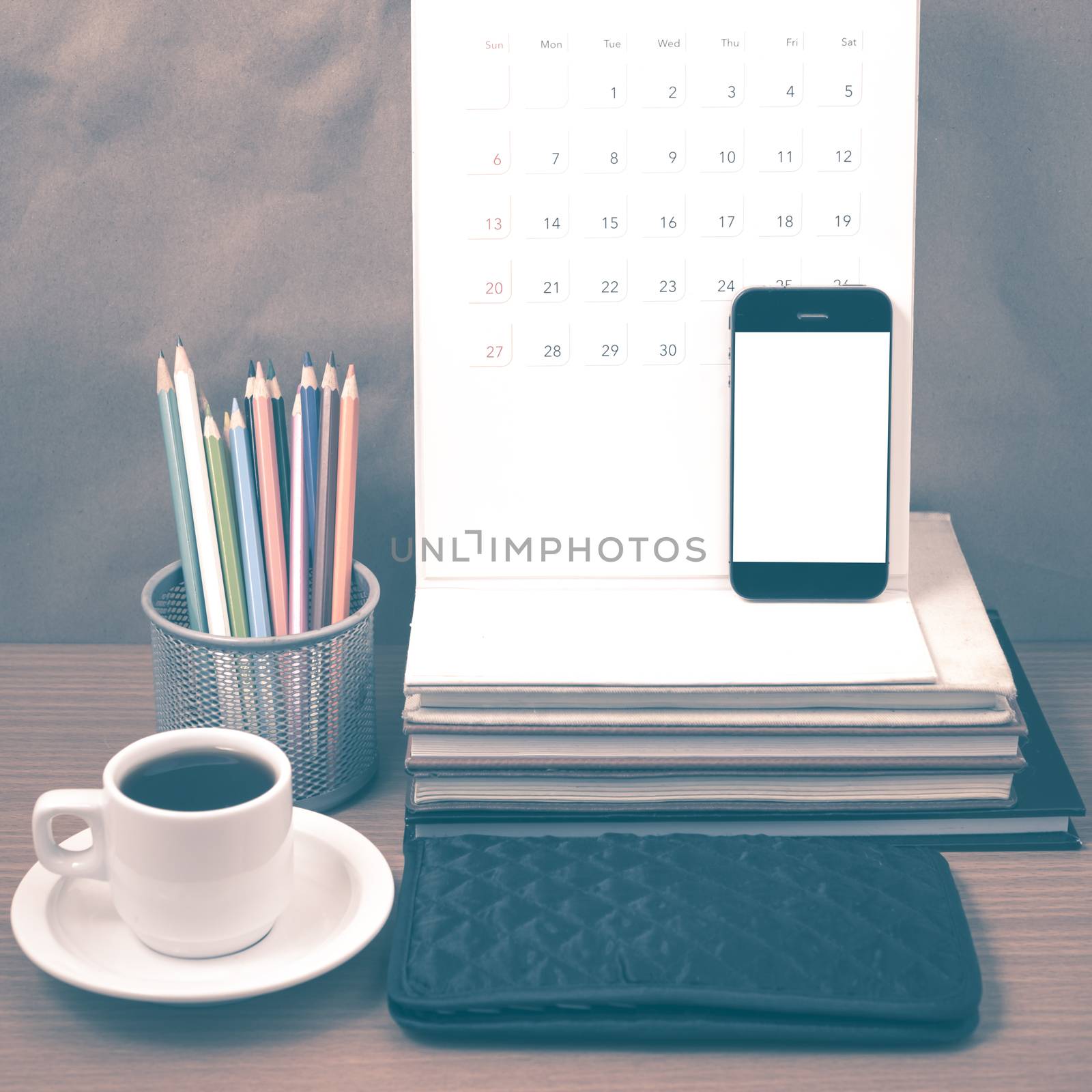 office desk : coffee with phone,wallet,calendar,color pencil box,stack of book on wood background vintage style