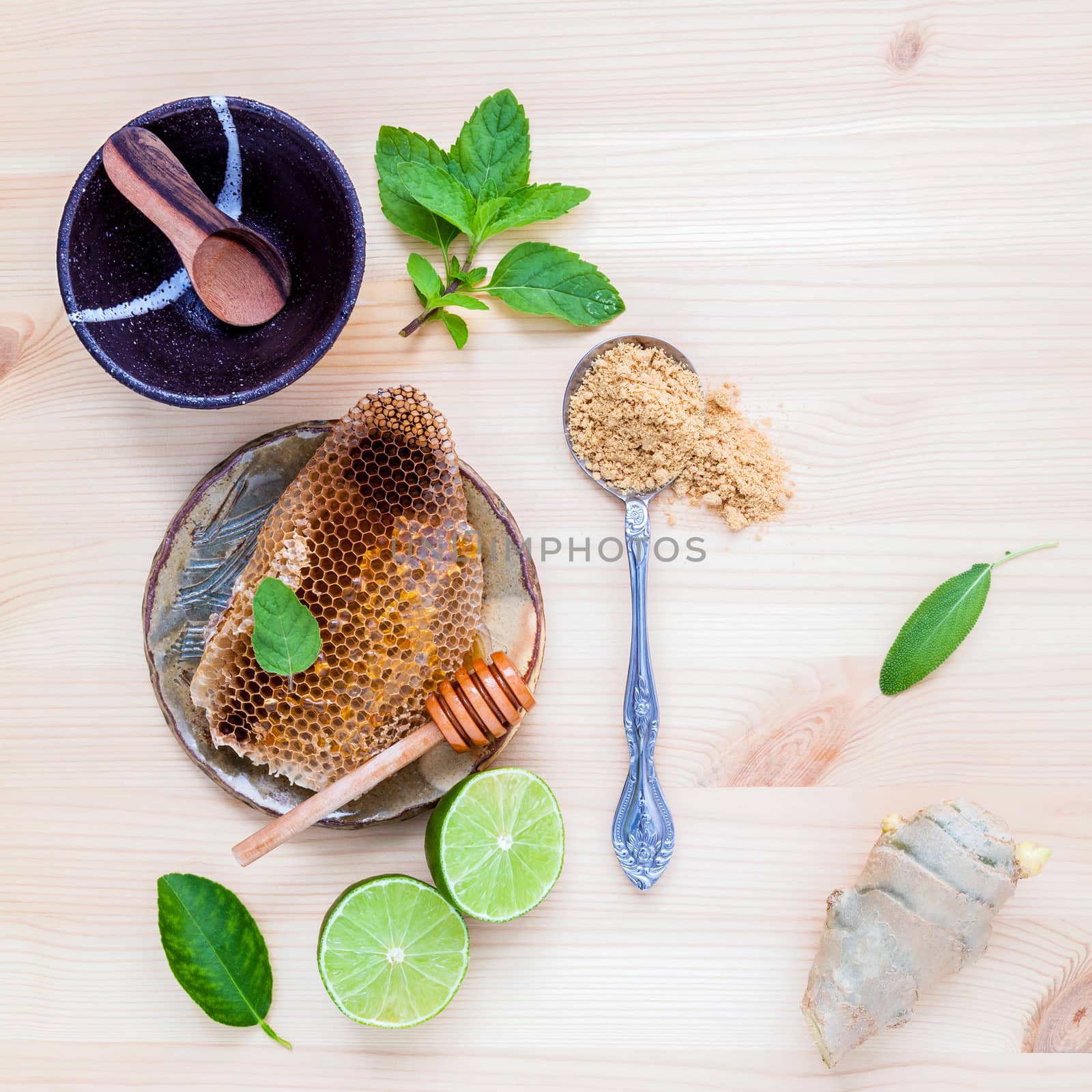 Honeycomb on ceramic plate with peppermint ,lime ,ginger and sage set up on white wooden background.
