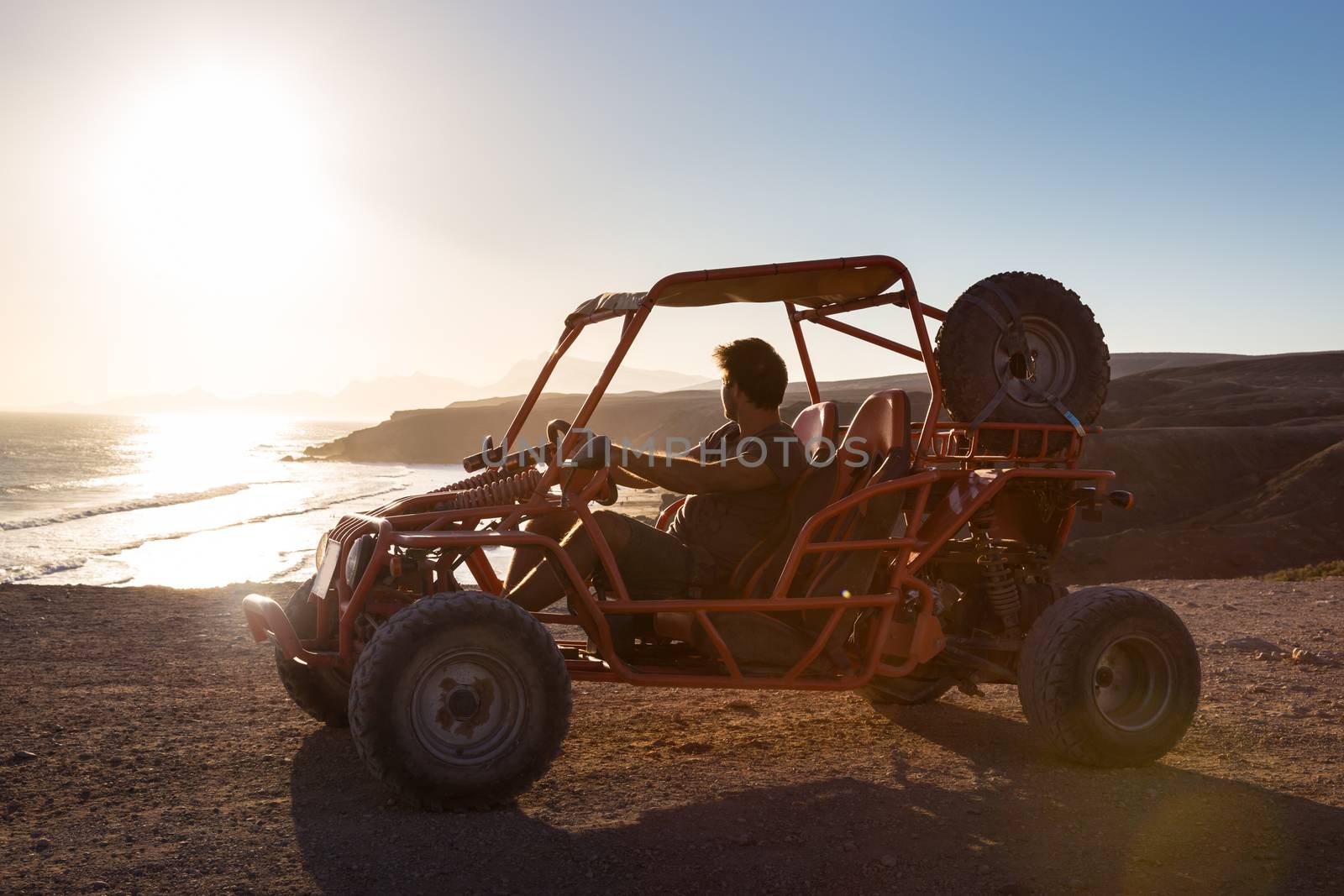 Active man driving quadbike on dirt road by the sea in sunset.