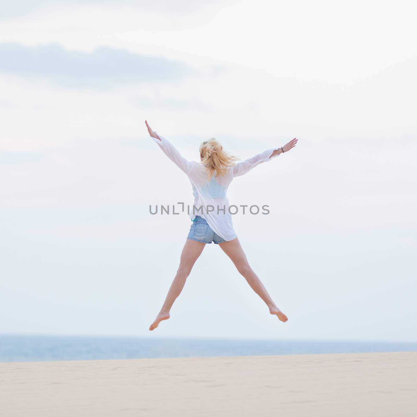 Relaxed woman enjoying freedom, feeling happy. Serene relaxing woman in pure happiness and elated enjoyment, jumping with arms outstretched up. Copy space for text.