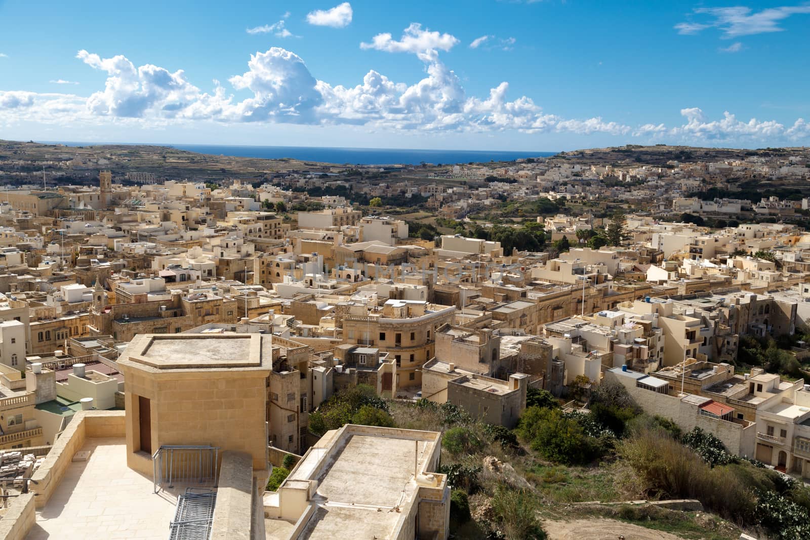 View of Victoria city in Malta, with historical limestone buildings, on cloudy blue sky background.
