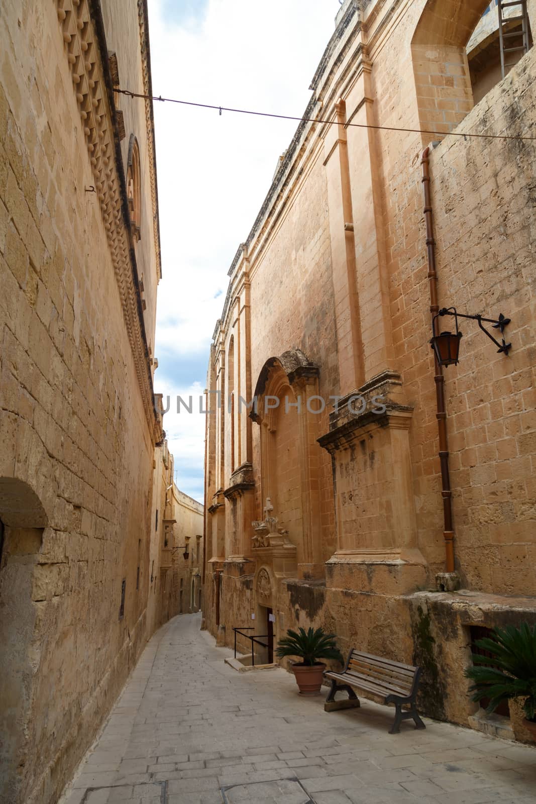 View of Mdina streets with limestone historical buildings around, on cloudy sky background.