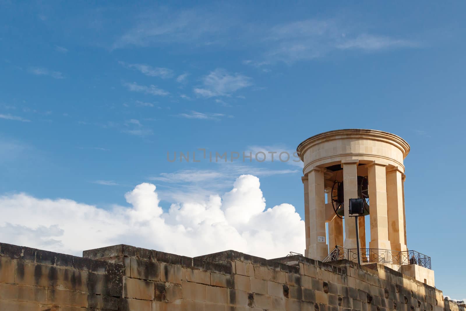 View of the bell tower of Siege Bell Memorial in Valletta, Malta, on cloudy blue sky background.