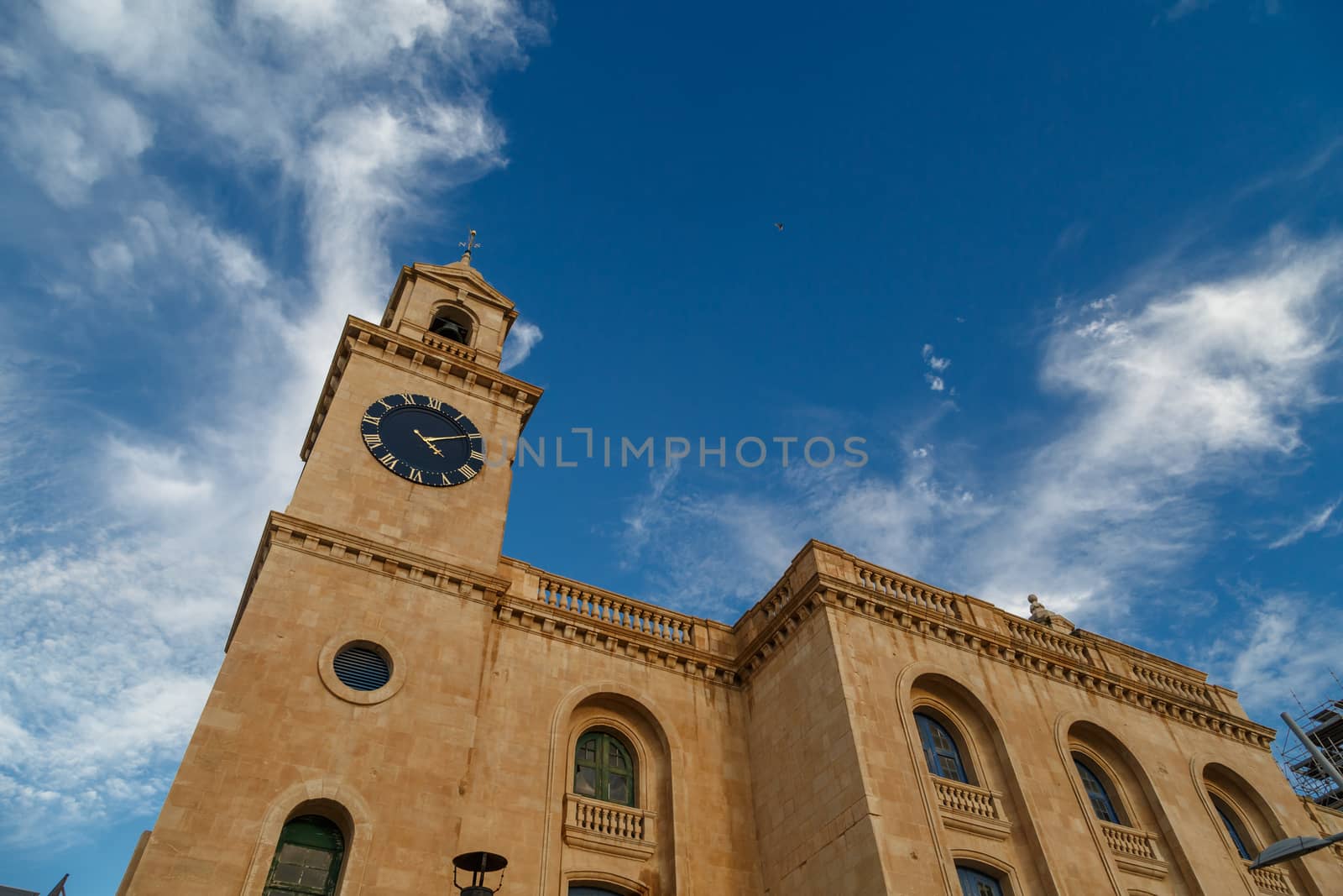 View of a church in Valletta Malta with limestone belfry clock tower, on cloudy blue sky background.