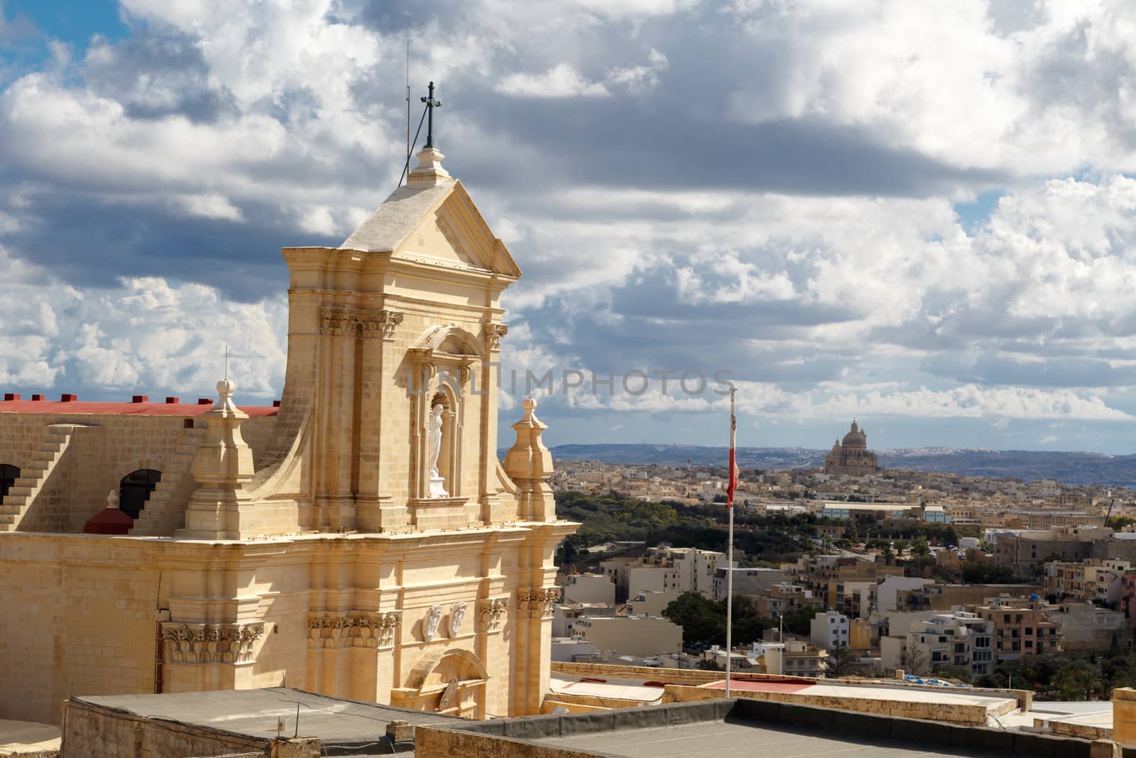View of a historical church in Victoria, Malta with a limestone belltower, on cloudy sky background.