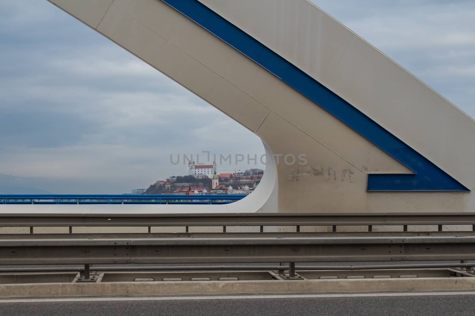 Shape of a modern bridge Apollo with a blue detail. In the background the downtown of Bratislava with the castle and cathedral. Intensively cloudy sky.