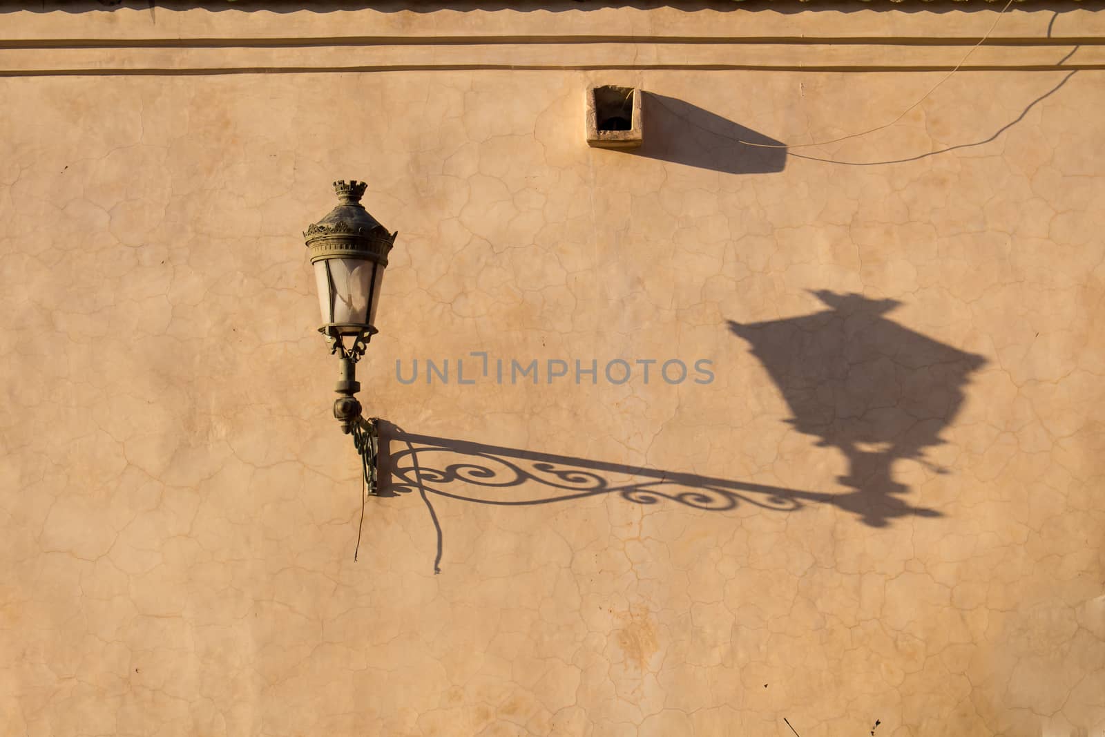 Old lantern on a dark yellow wall in the medina of Marrakesh. Long shadow during the golden hour.