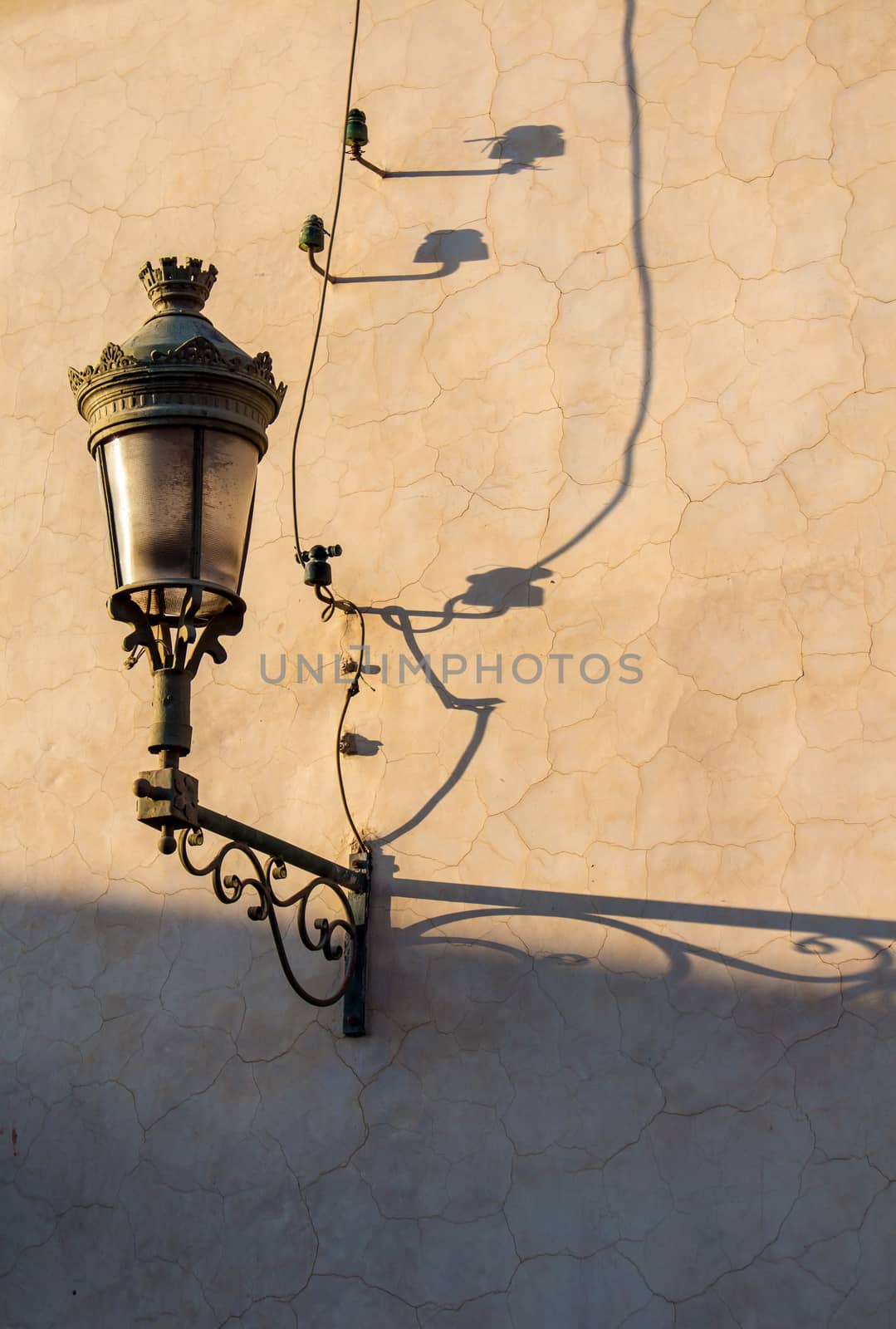 Old lantern on a dark yellow wall in the medina of Marrakesh. Long shadow during the golden hour.