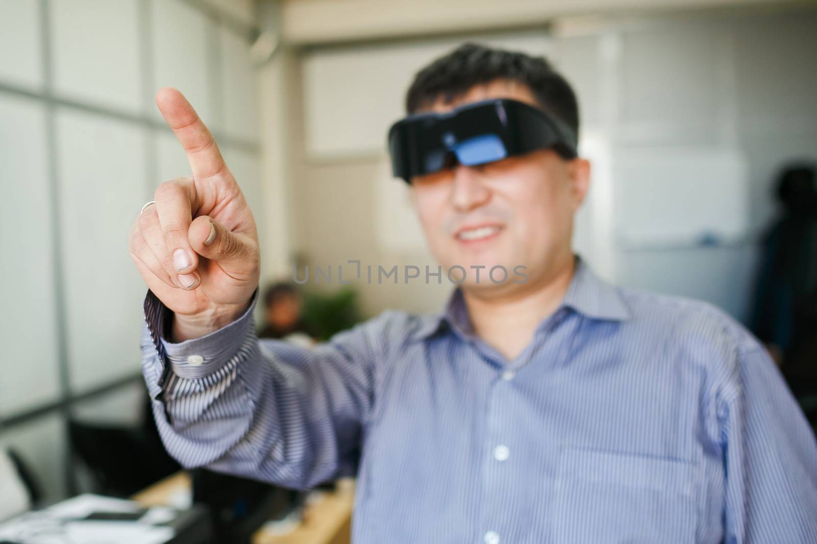 A man in a virtual reality helmet points finger up in the air inside the office premises.