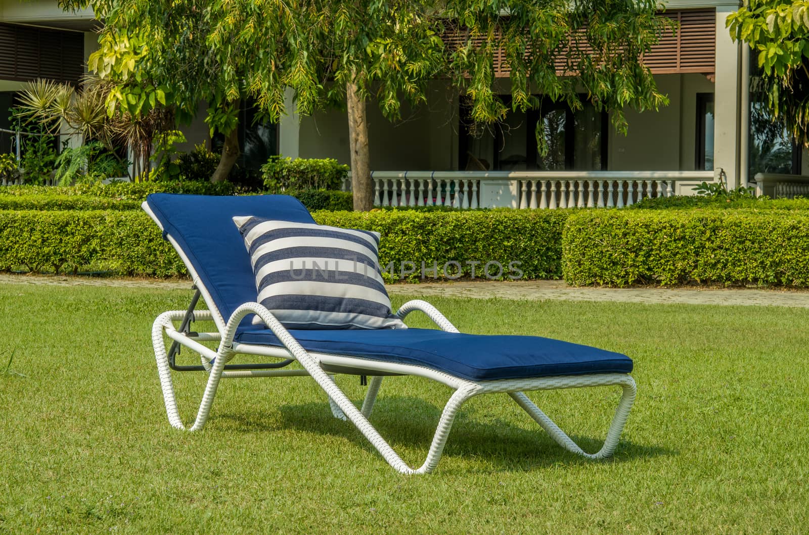 Rattan sun lounger with blue cushion in the green garden