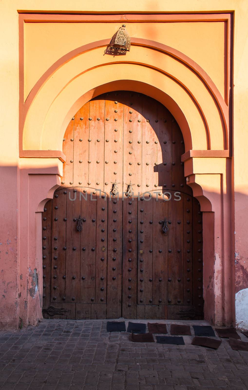 Heavy wooden gate with traditional decoration. Arch on the top. Warm colors during the golden hour. Medina of Marrakesh, Morocco.