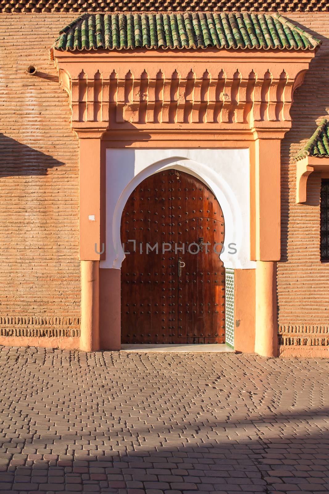 Heavy wooden gate with traditional decoration. Arch on the top. Warm colors during the golden hour. Medina of Marrakesh, Morocco.