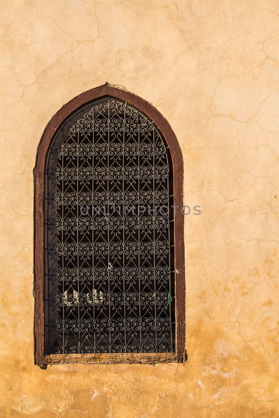 Traditional arabian window with an arch and ornamental lattice. Light orange wall, during golden hour. Medina in Marrakesh, Morocco.