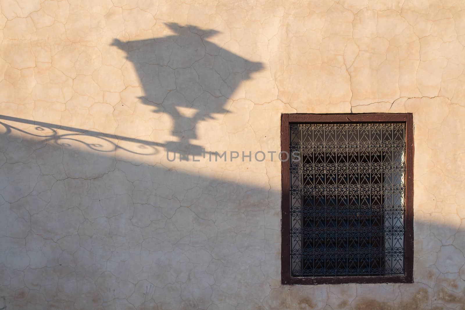 Old wall during the golden hour with a shadow of the old lantern and traditional window with lattice. Marrakesh, Morocco.