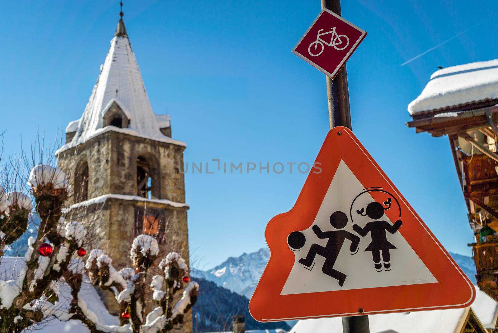 A boy and a girl playing on a roadsign close to a school, with a snow-covered church and mountains in the background.