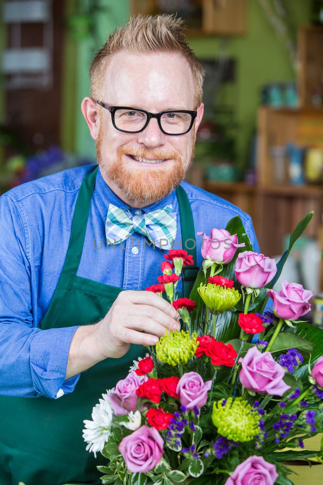 Dapper man wearing eyeglasses and apron creating a flower arrangement