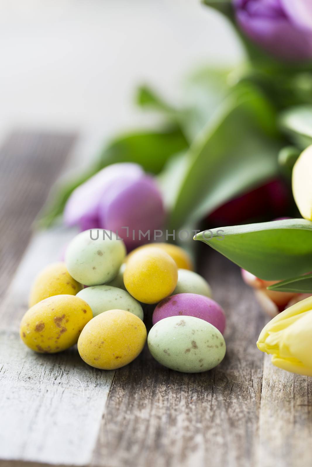 Close up of milk chocolate eggs on table with flowers vertical orientation.