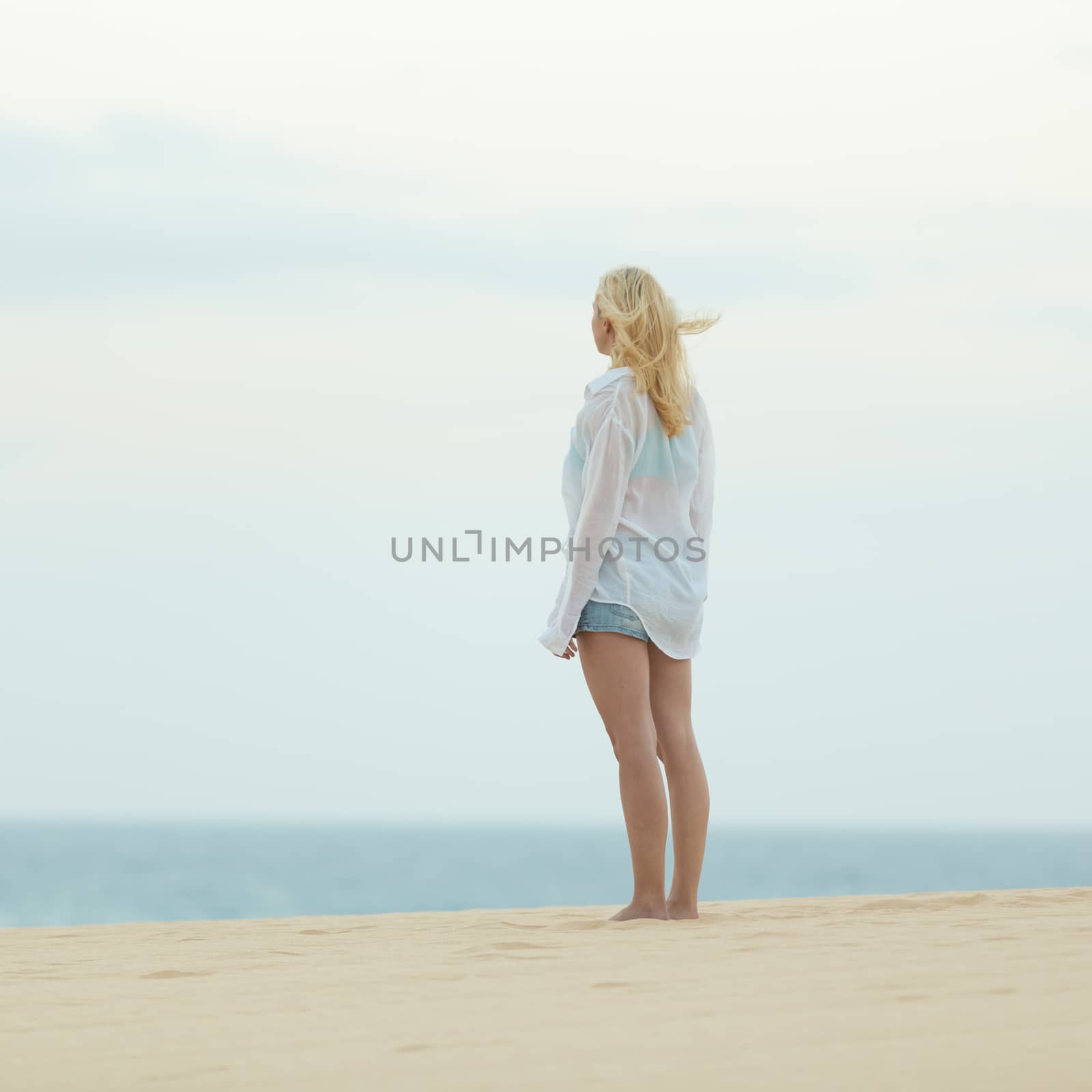 Woman on sandy beach in white shirt at dusk.  by kasto