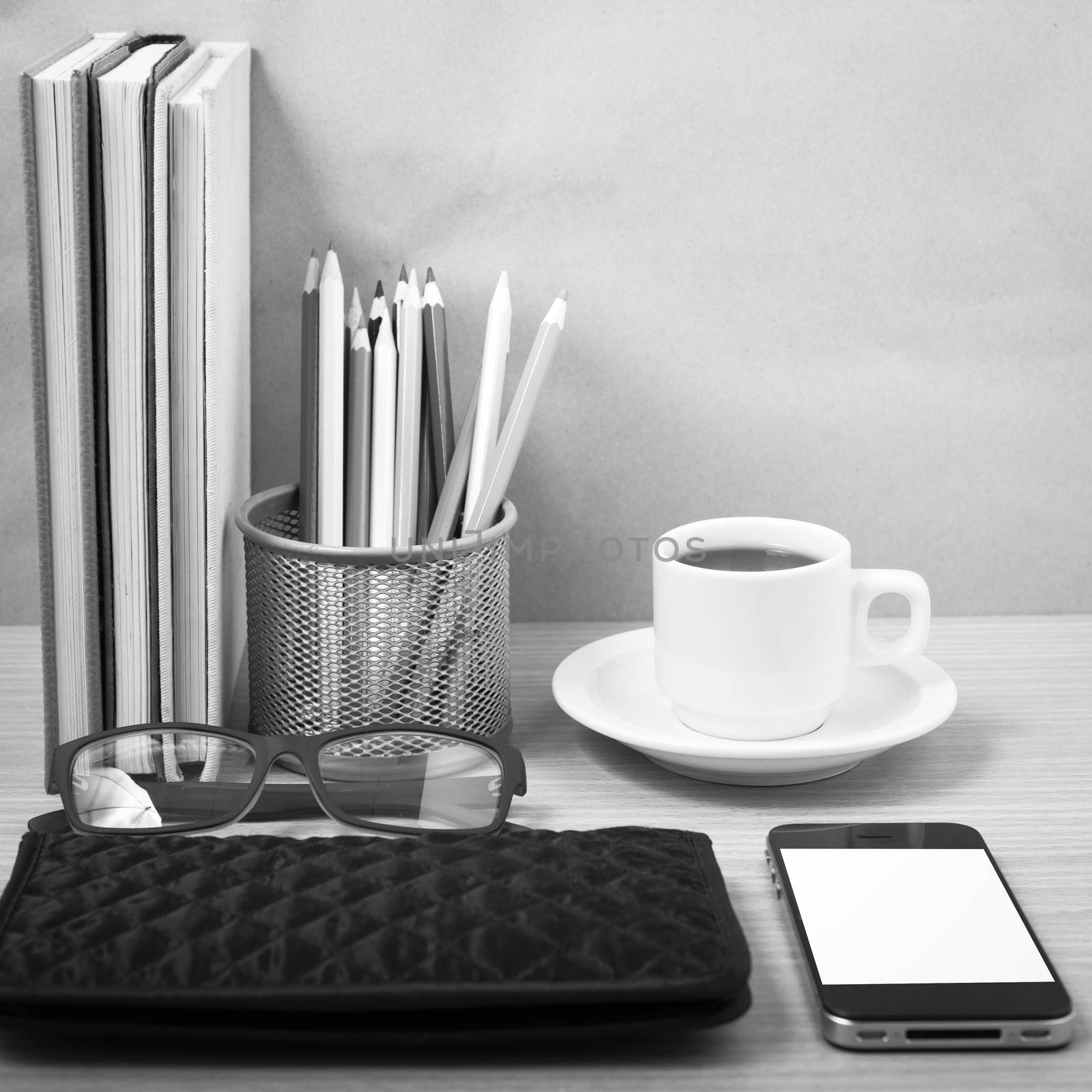 office desk : coffee with phone,stack of book,eyeglasses,wallet,color pencil box on wood background black and white color