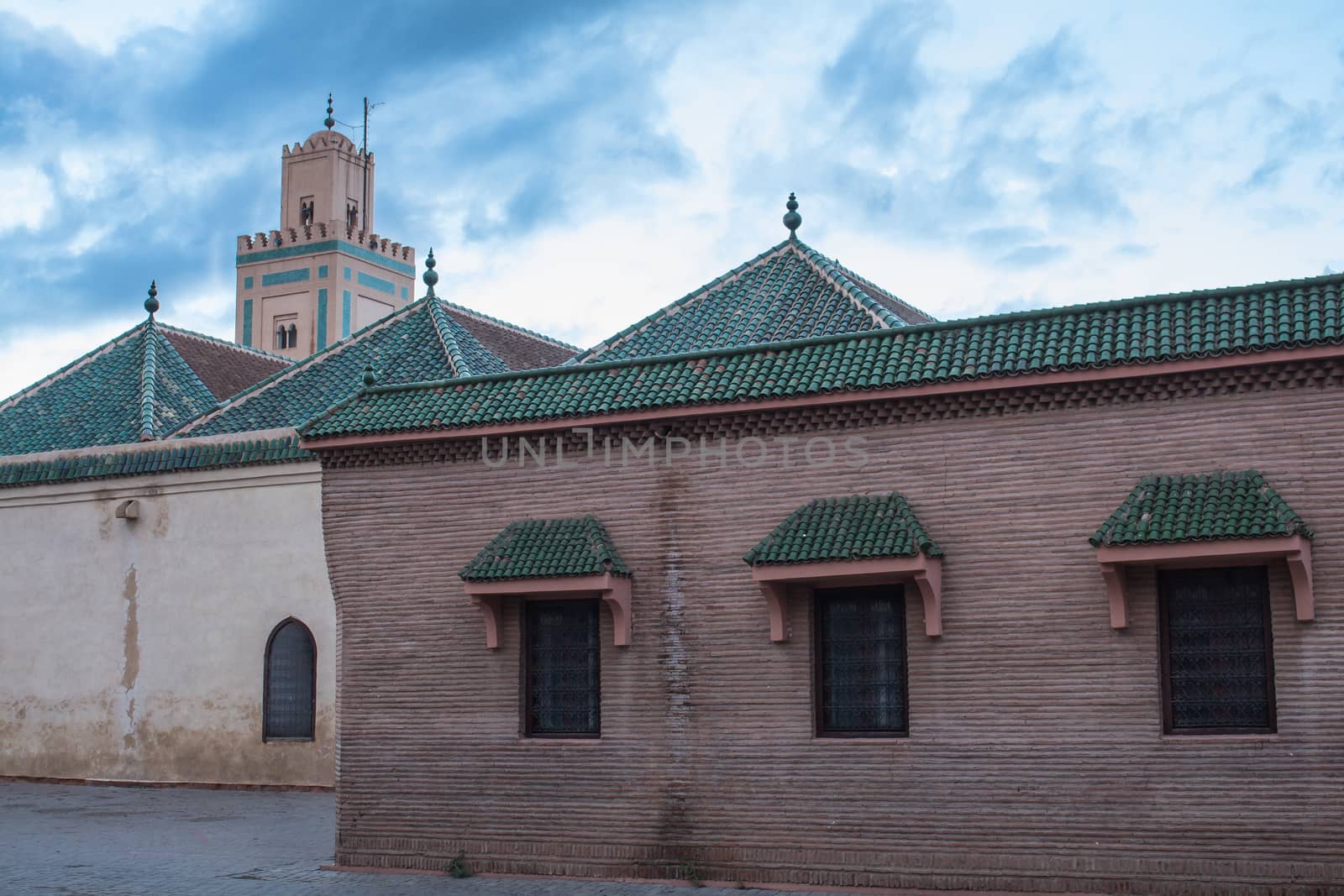 Streets still empty during dawn. Buildings and tower of the Ben Youssef Mosque in the medina of Marrakesh. Cloudy morning sky.