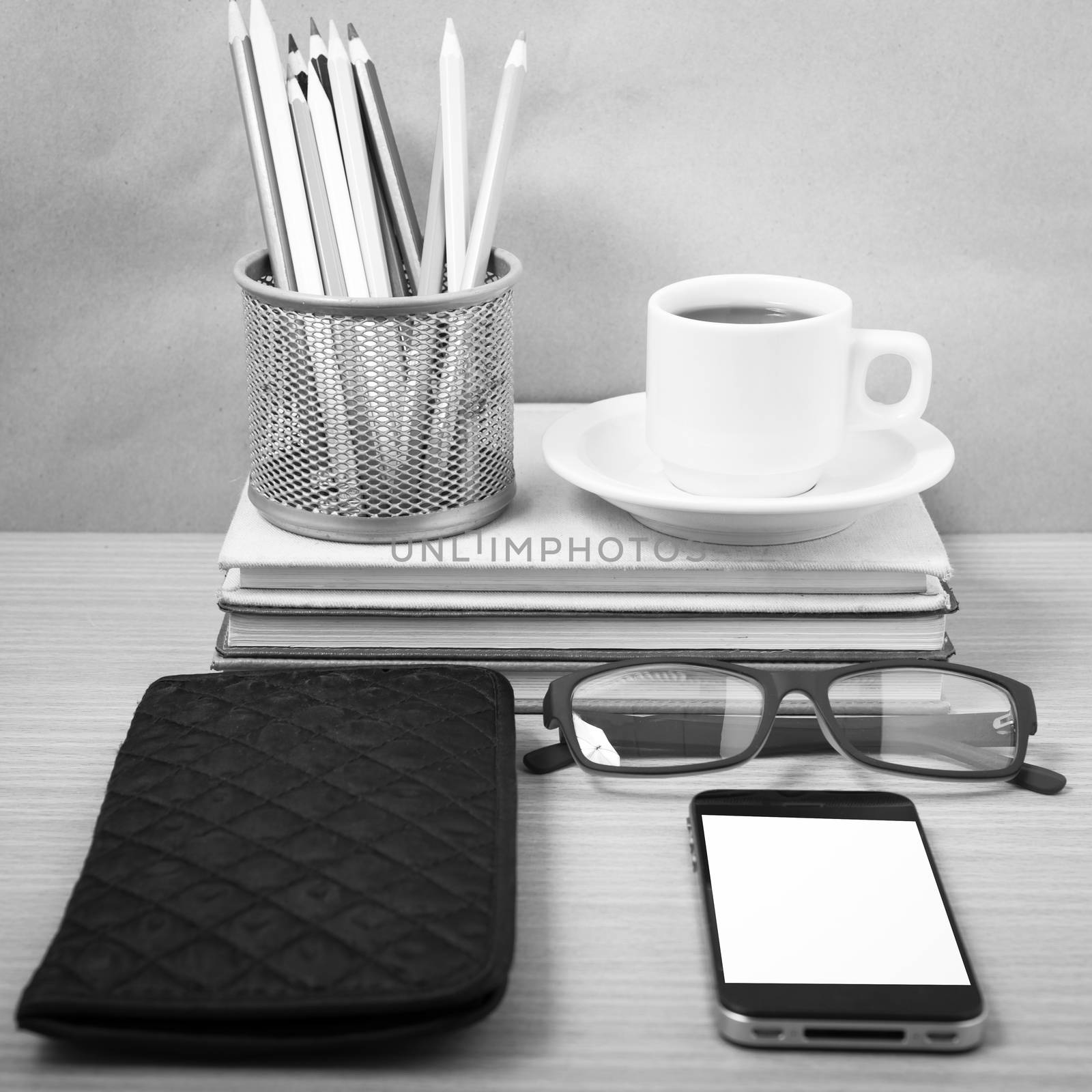 office desk : coffee with phone,stack of book,eyeglasses,wallet,color pencil box on wood background black and white color