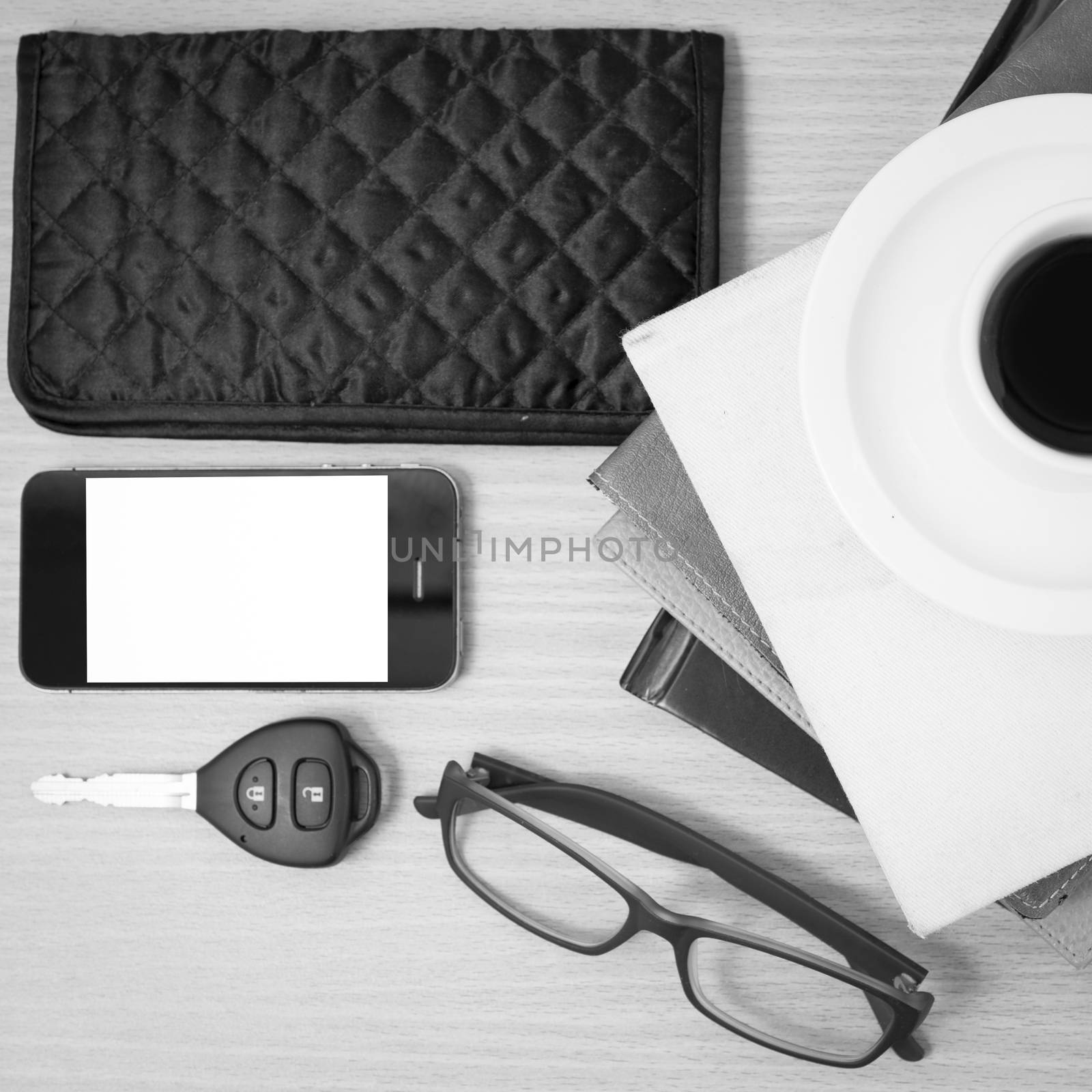 coffee and phone with stack of book,car key,eyeglasses and wallet on wood background black and white color