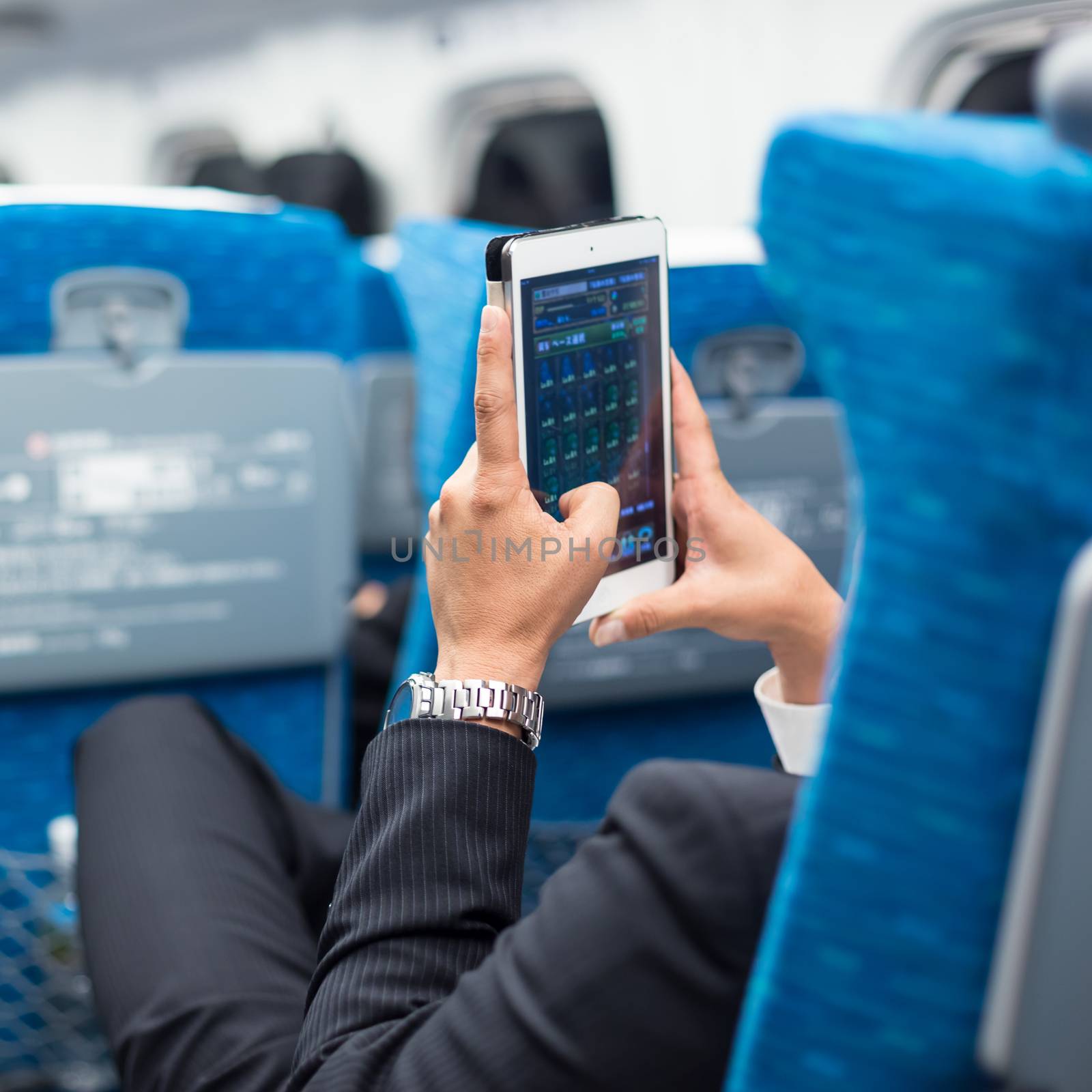 Businessman using tablet phone on airplane. by kasto