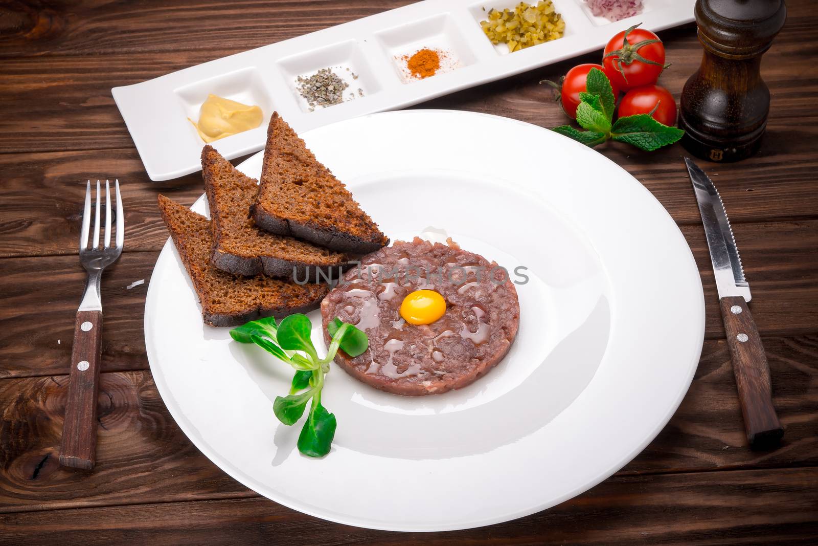 Beef tartare with spices and seasoning on wooden background