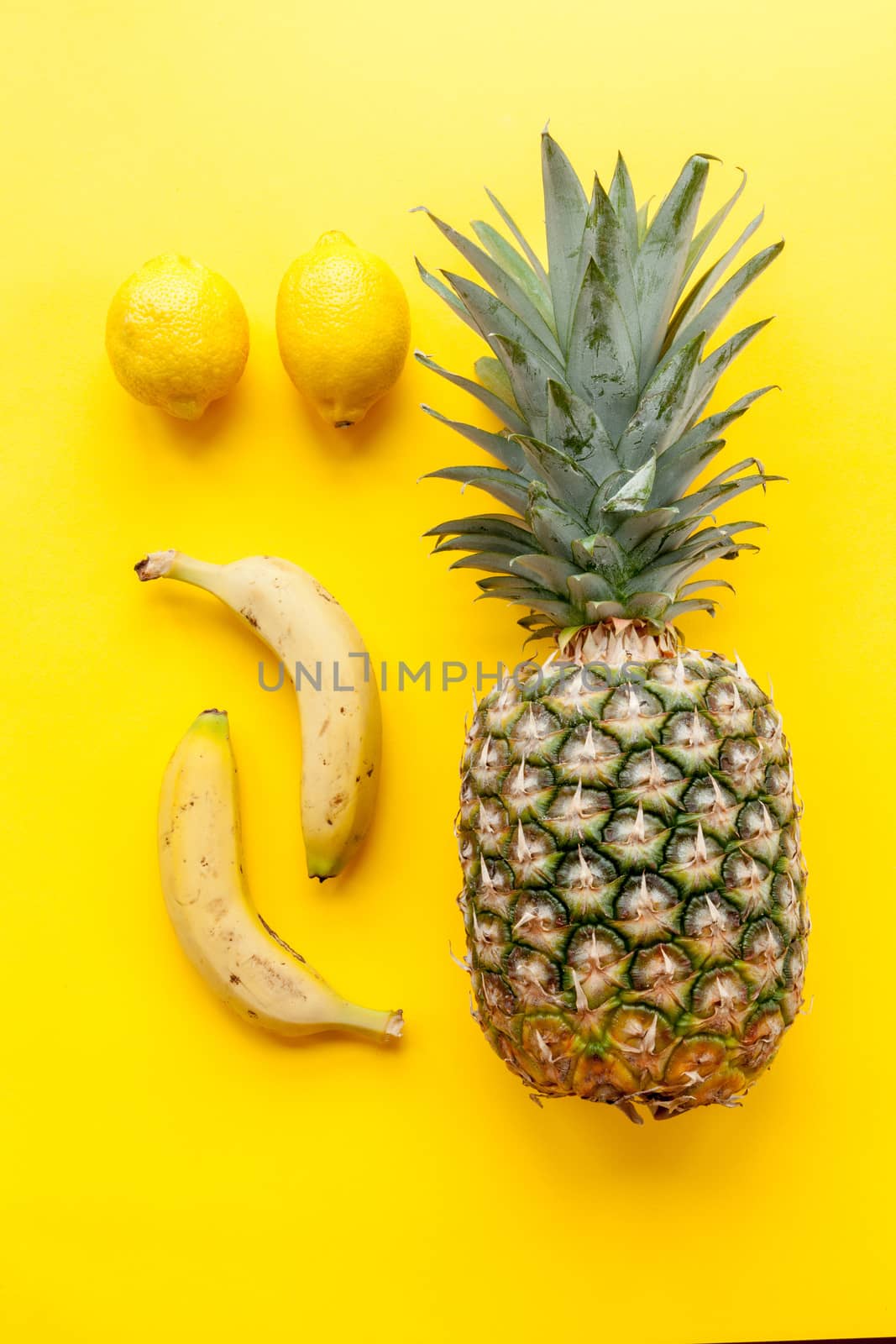 Natural and complete pineapple, bananas and lemons on a yellow background and flat