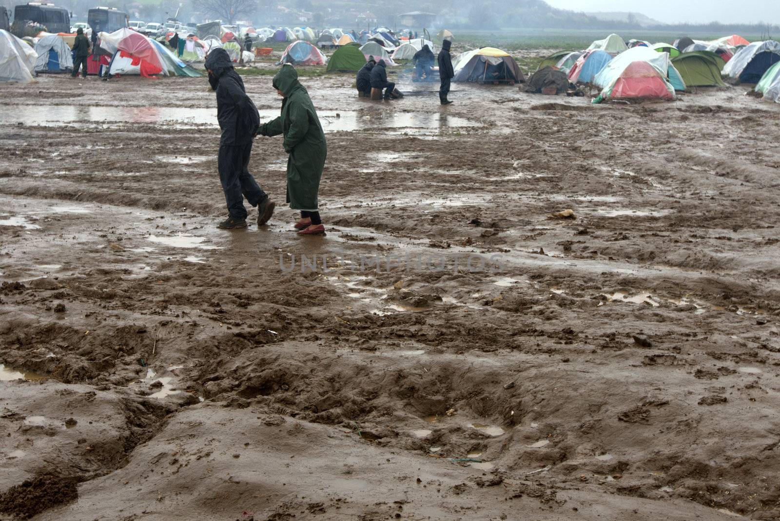 GREECE, Idomeni: Two people walk in mud as thousands of migrants are stranded in a makeshift camp for migrants and refugees at the Greek-Macedonian border near the village of Idomeni on March 23, 2016. The UN refugee agency harshly criticized an EU-Turkey deal on curbing the influx of migrants to Greece, saying reception centers had become detention facilities, and suspended some activities in the country. The EU and Ankara struck a deal aiming to cut off the sea crossing from Turkey to the Greek islands that enabled 850,000 people to pour into Europe last year, many of them fleeing the brutal war in Syria.