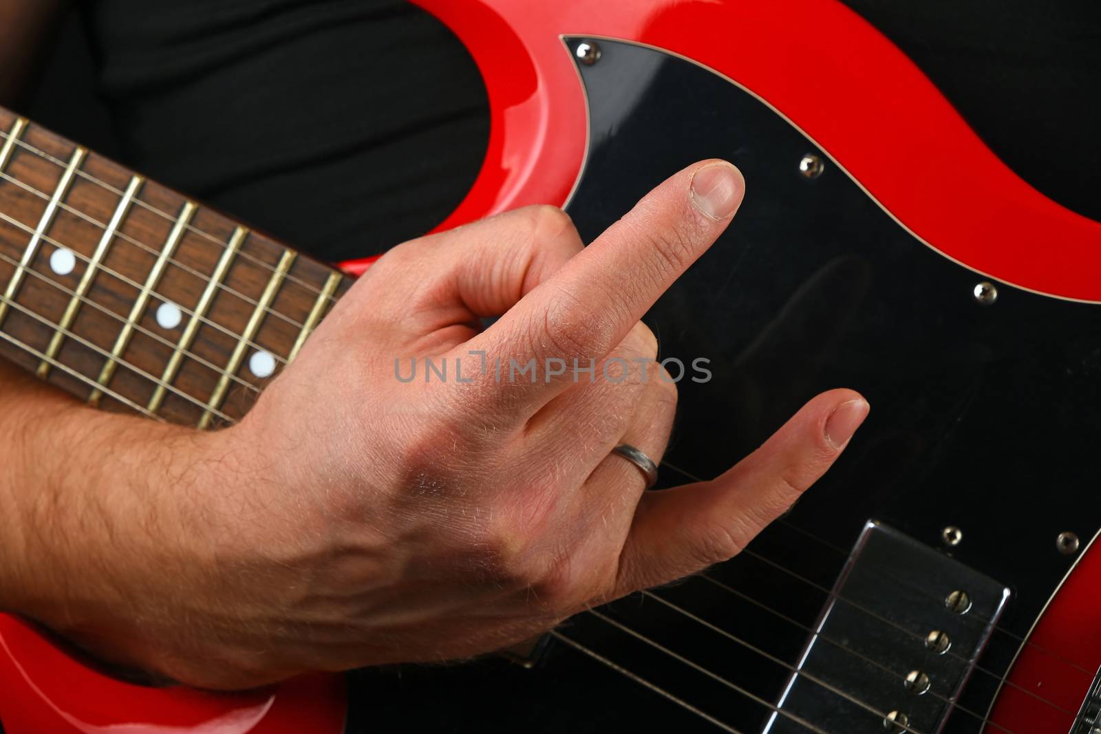 Hand with red guitar and devil horns isolated on black by BreakingTheWalls