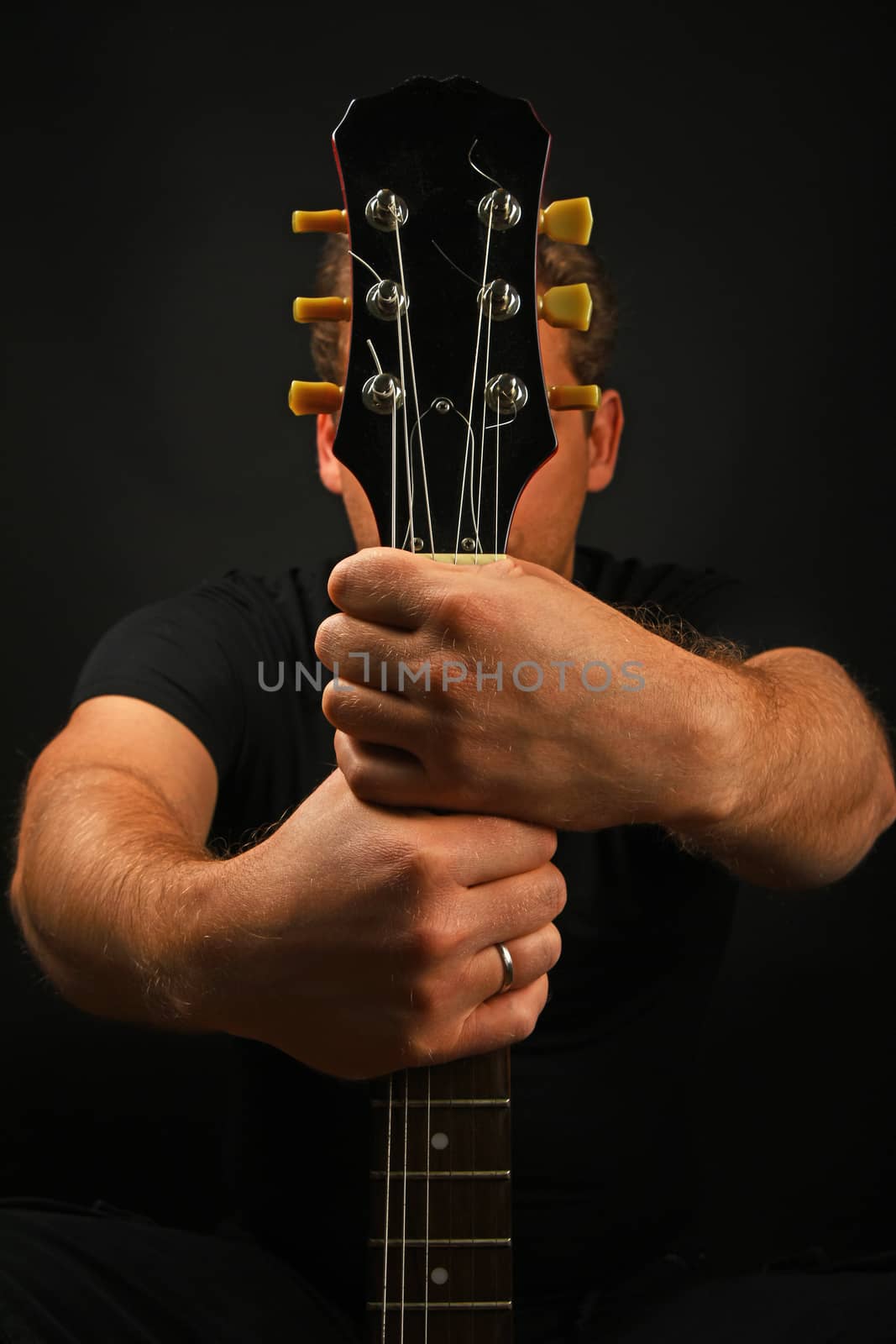Man sitting and holding guitar neck with two hands isolated on black background