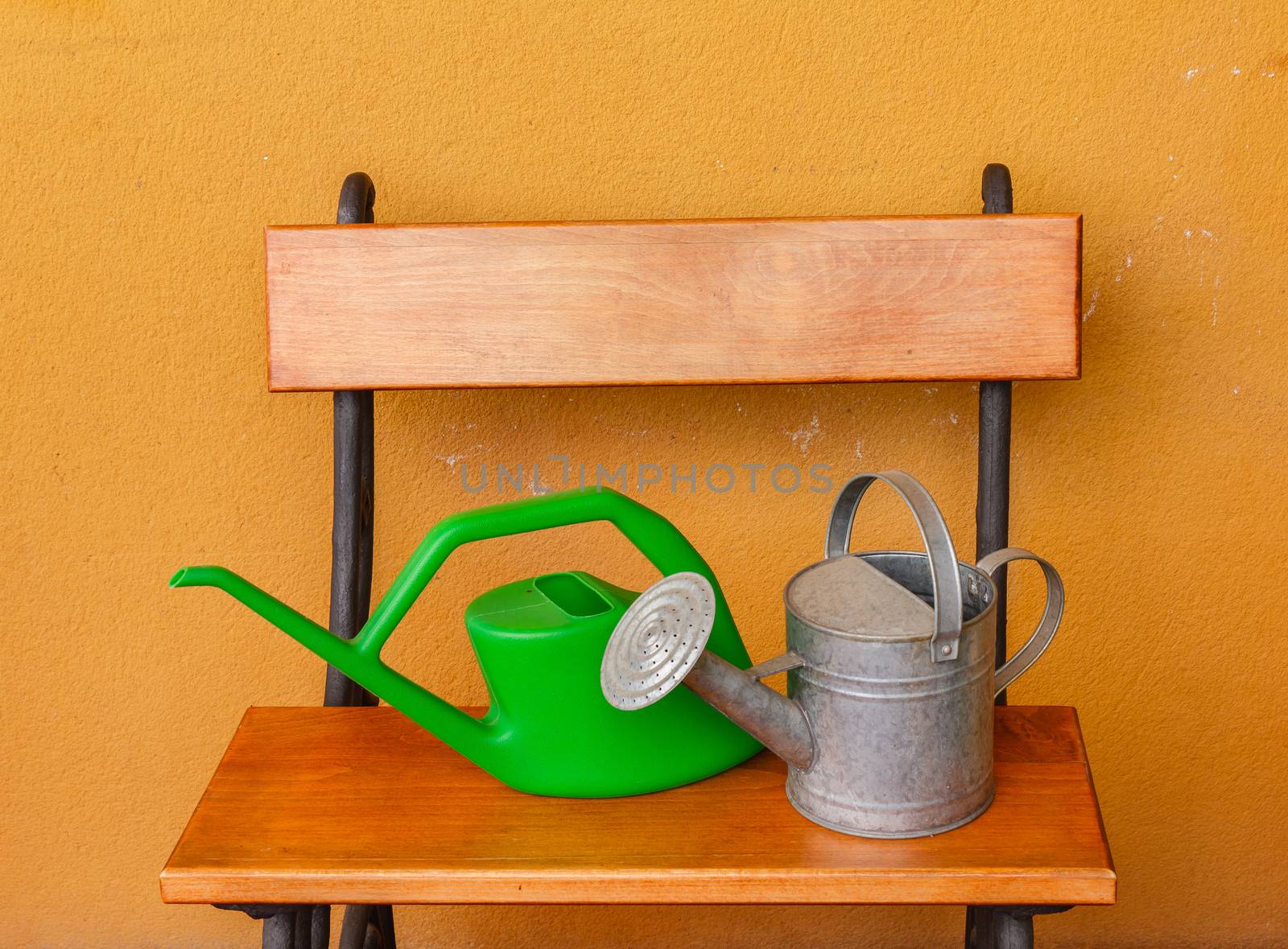a watering can of  aluminium and a plastic one laid on wooden be by moorea