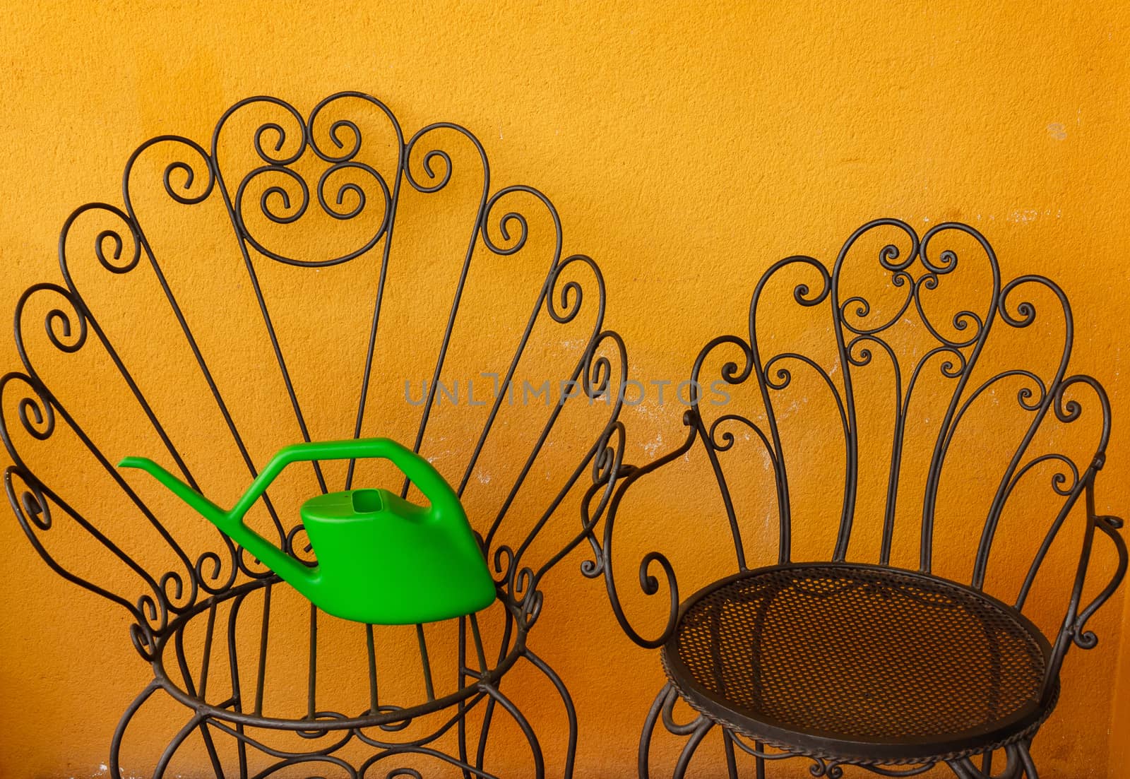 a corner of the  terrace with two iron chairs  with a plastic green watering-can
