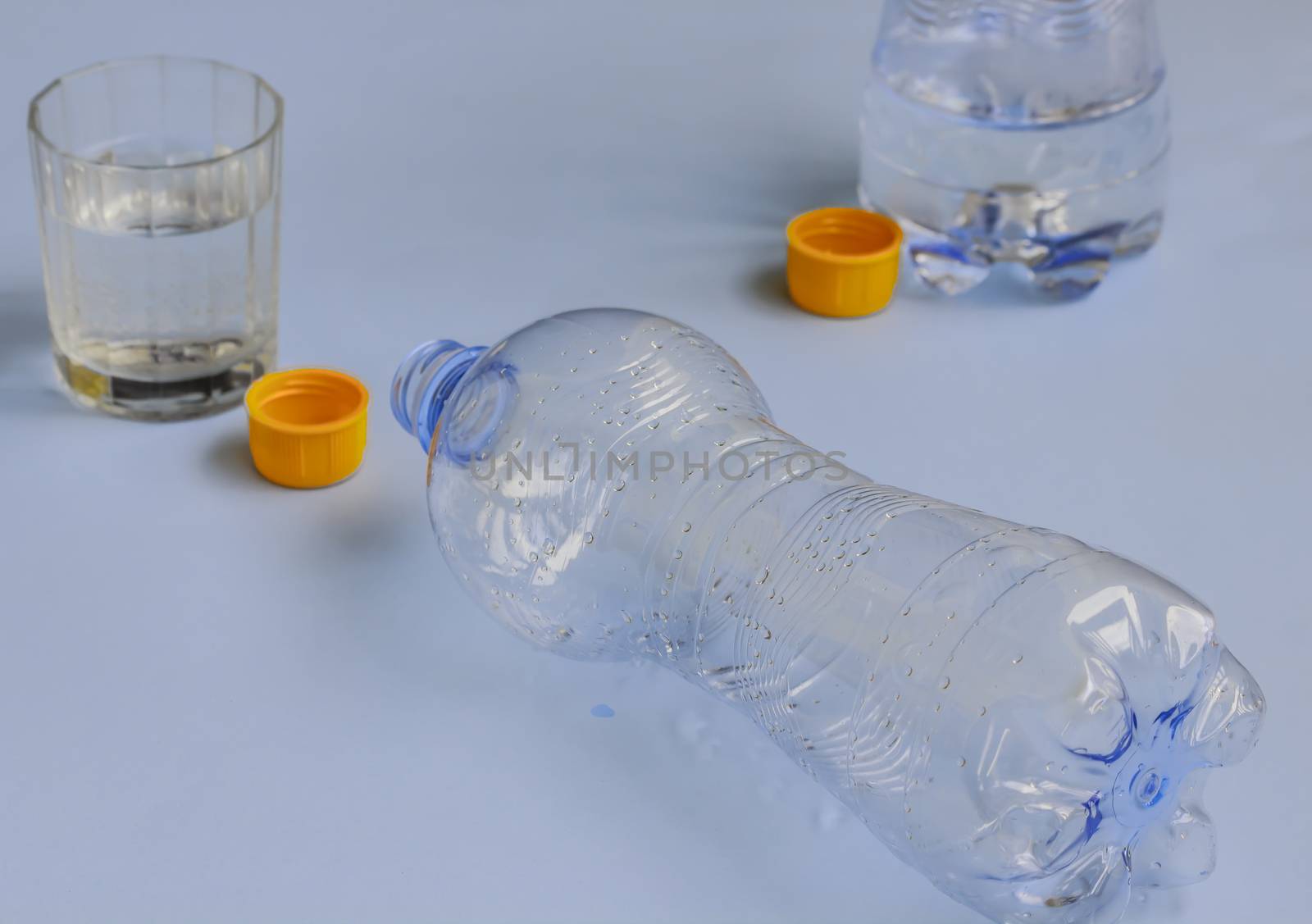 two bottles of water drained ,with orange cap and the glass