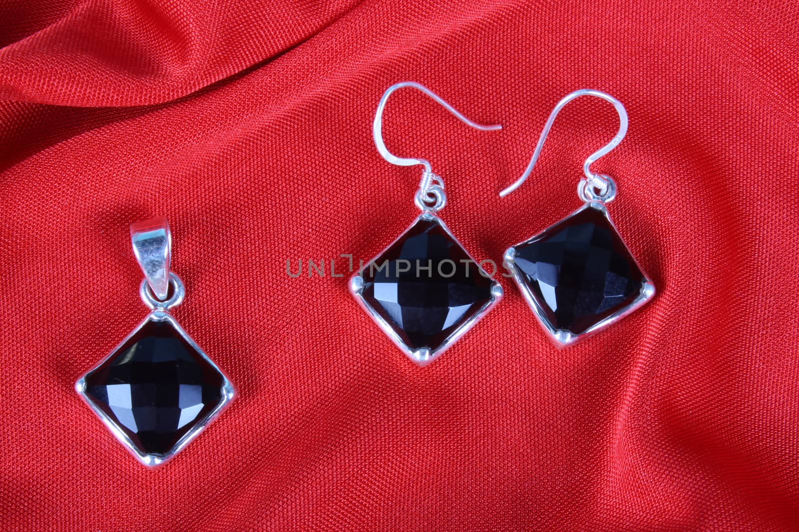 A set of black onyx jewelery made in silver consisting of a pendant and a pair of earrings, on red fabric.