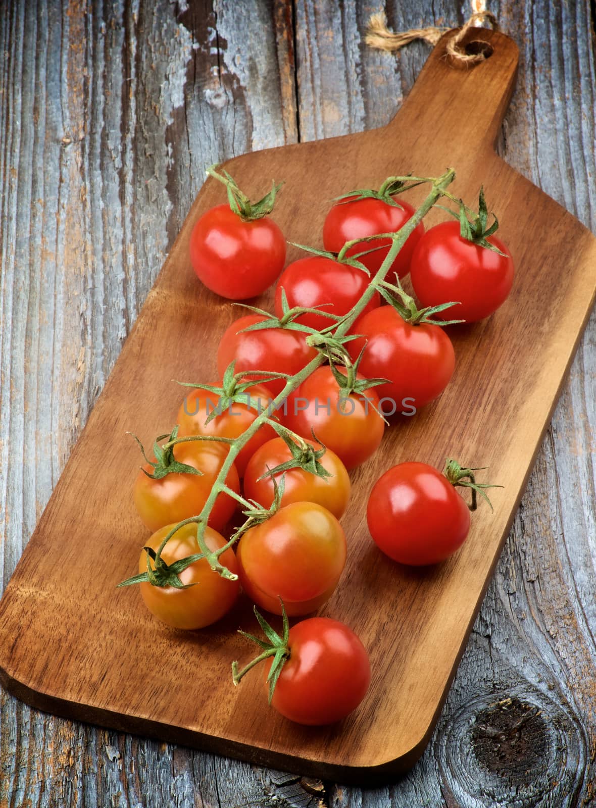 Branch of Ripe Raw Cherry Tomatoes on Wooden Cutting Board closeup on Rustic Wooden background