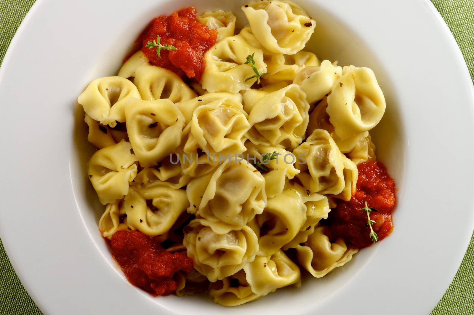 Delicious Meat Cappelletti in with Tomatoes Sauce in White Plate closeup on Green Napkin background