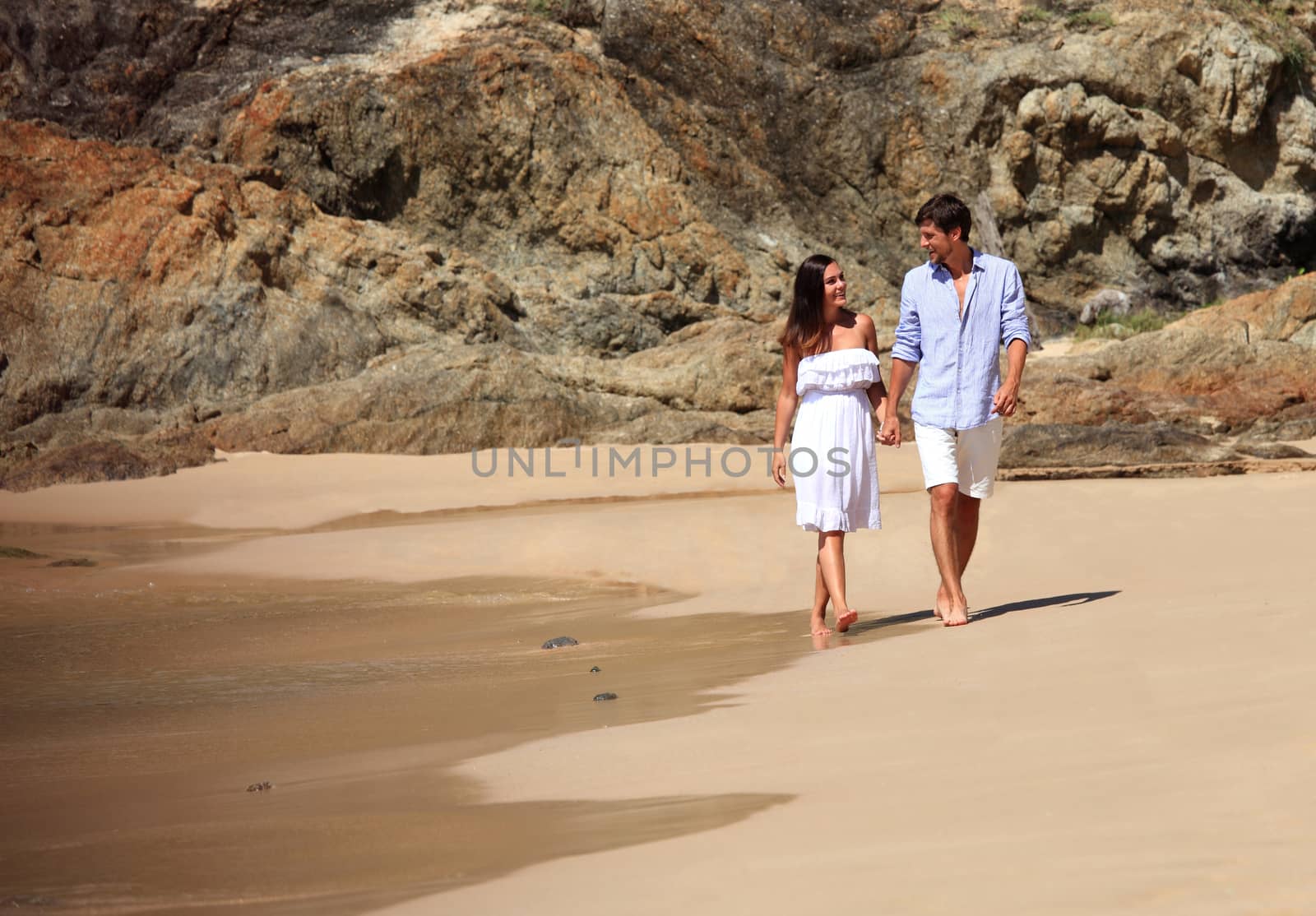 Cheerful couple walking on beach on rock background