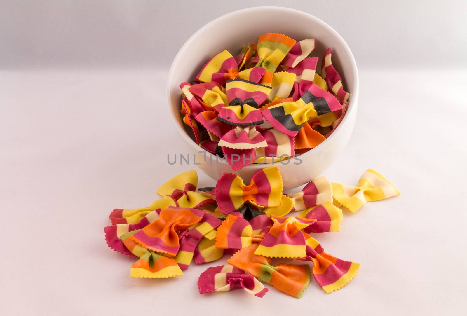 overflowing bowl of colourful pasta bows against a white background