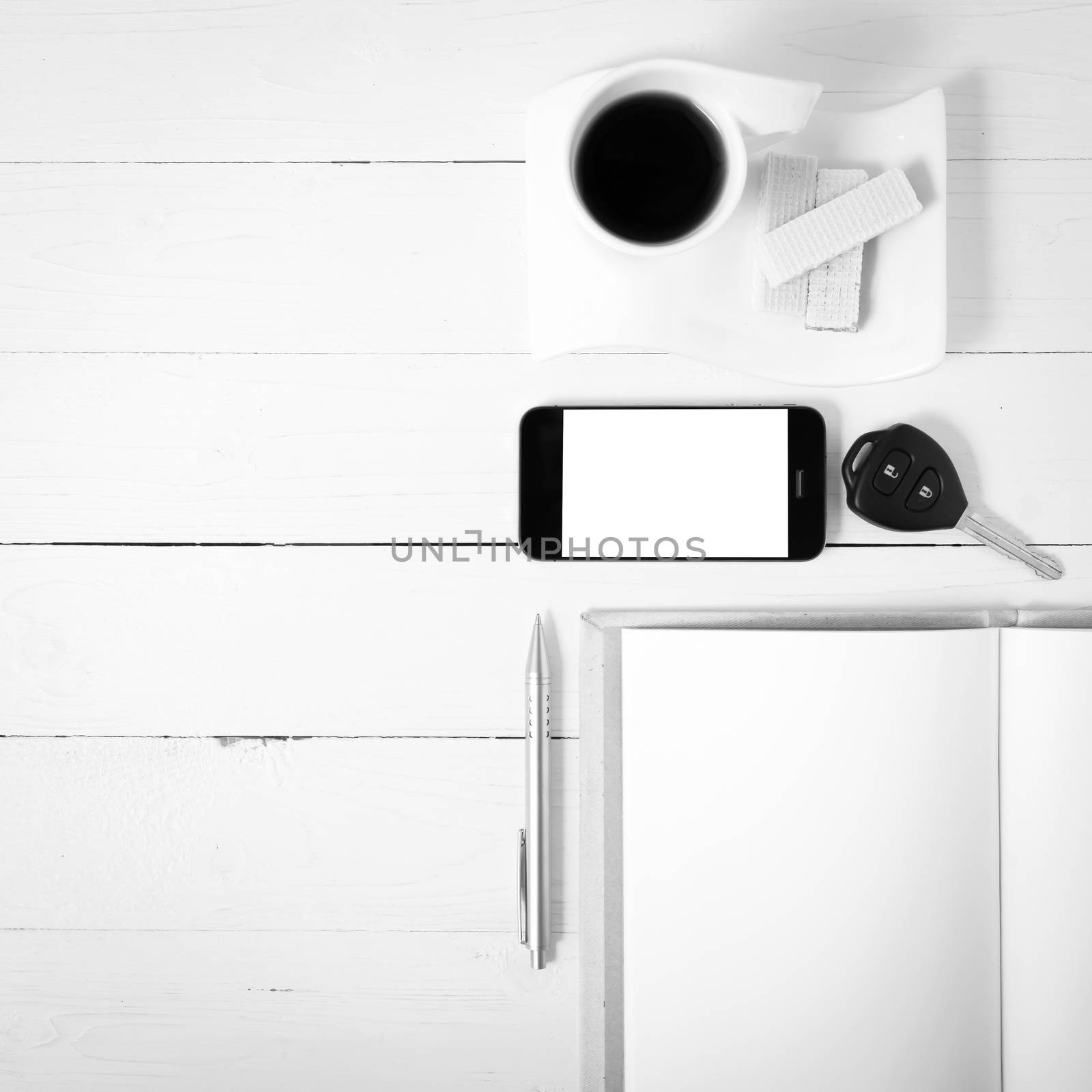 coffee cup with wafer,phone,car key,notebook on white wood background black and white color