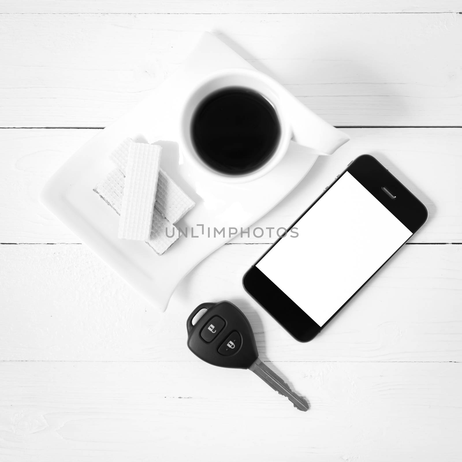 coffee cup with wafer,phone,car key on white wood background black and white color