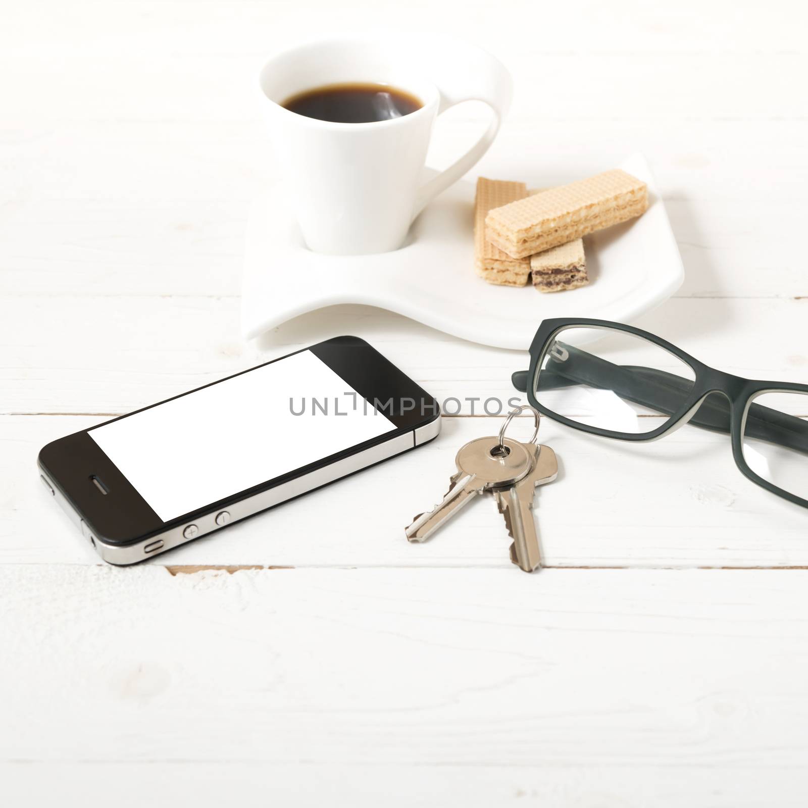 coffee cup with wafer,phone,key,eyeglasses on white wood background