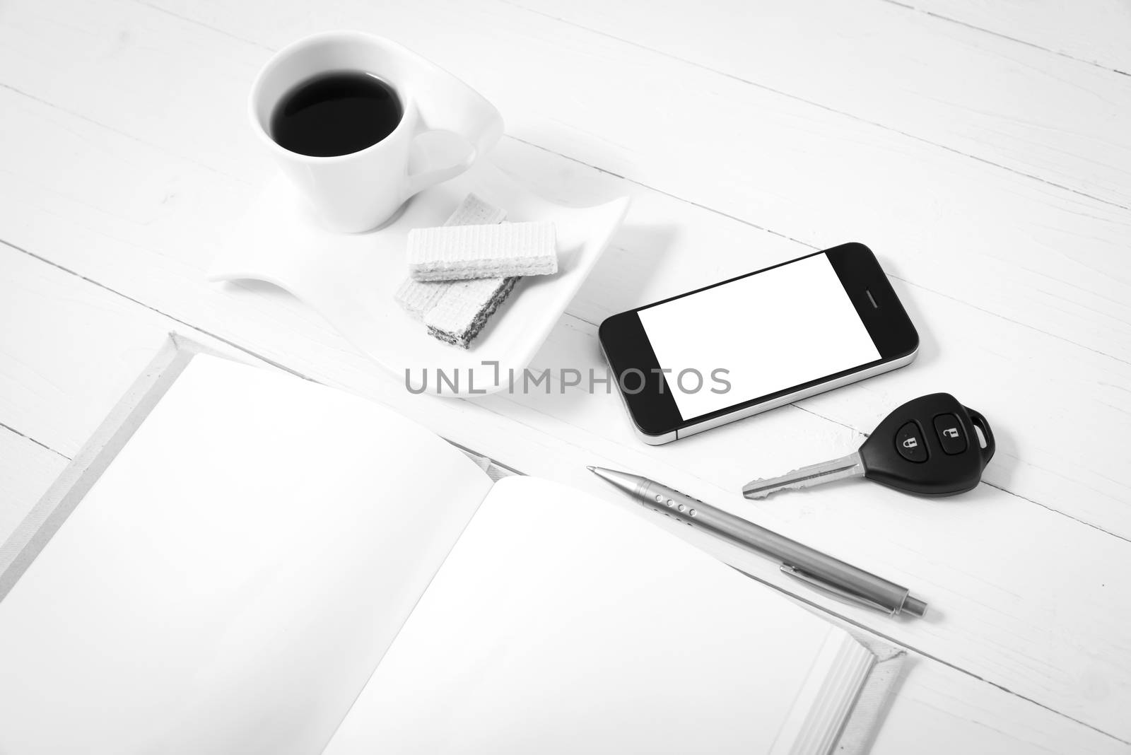 coffee cup with wafer,phone,car key,notebook on white wood background black and white color