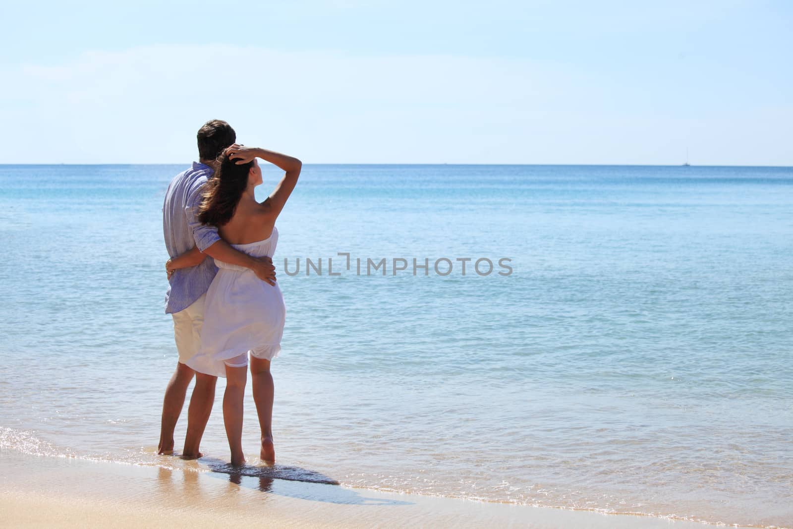 Couple on beach look at horizon over the sea