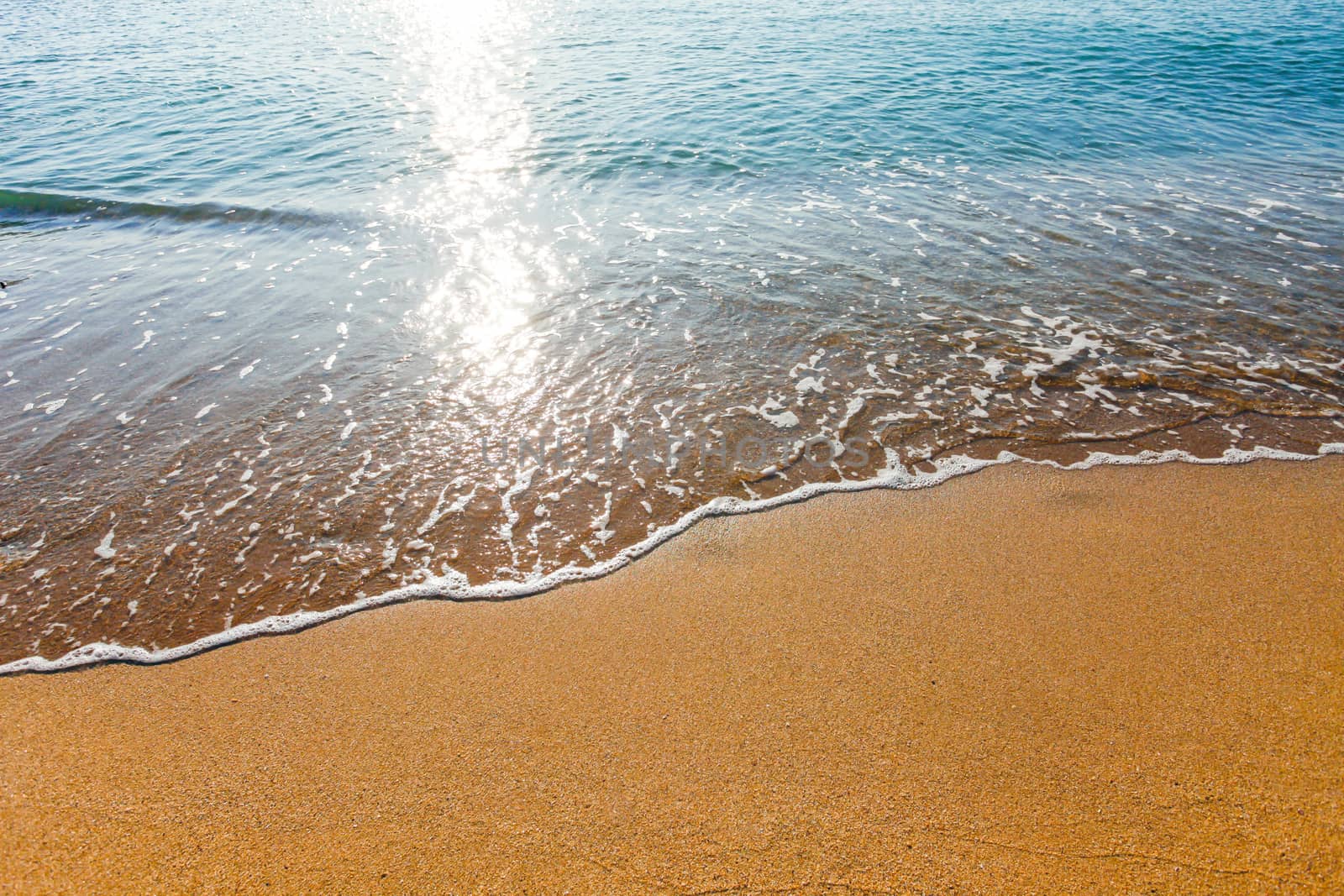 Sun light reflected on soft wave of the sea on the sandy beach