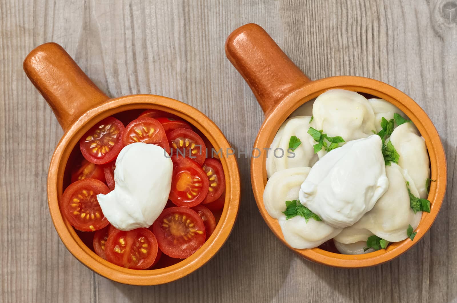 Chopped tomatoes and dumplings with sour cream, in a ceramic Cup on old wooden surface.